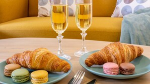 A table with croissants, macarons, and two glasses of a yellow beverage, set on a wooden table with a yellow sofa in the background. - Welcome Apartment, in the center of Malaga! (Málaga)