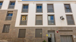 A multi-story building with a white facade, multiple windows with metal grilles, a door with a red fire alarm, and a small potted plant on the ground floor. - Welcome Apartment, in the center of Malaga! (Málaga)