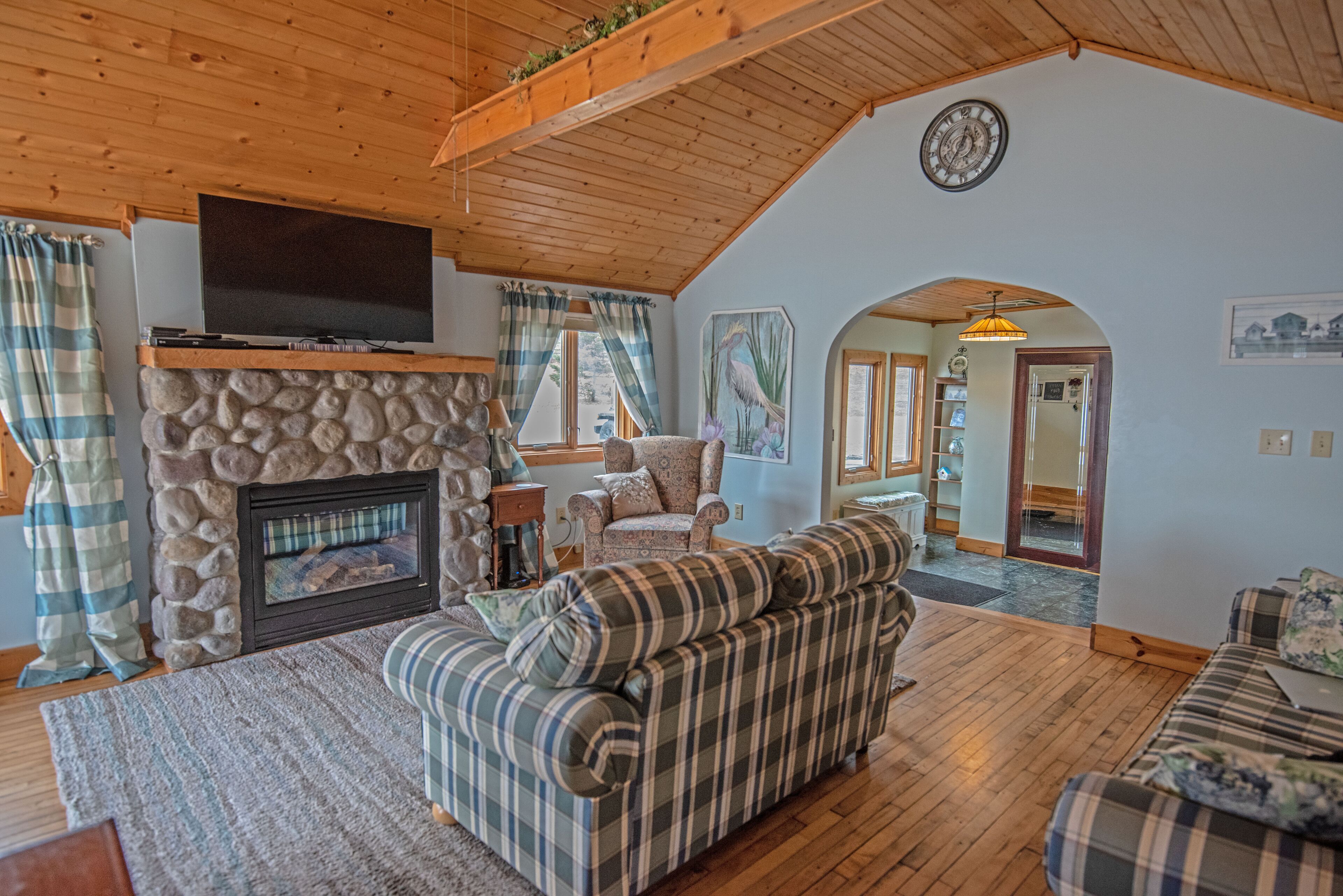 A cozy living room with a stone fireplace, plaid sofas, and a wooden ceiling.