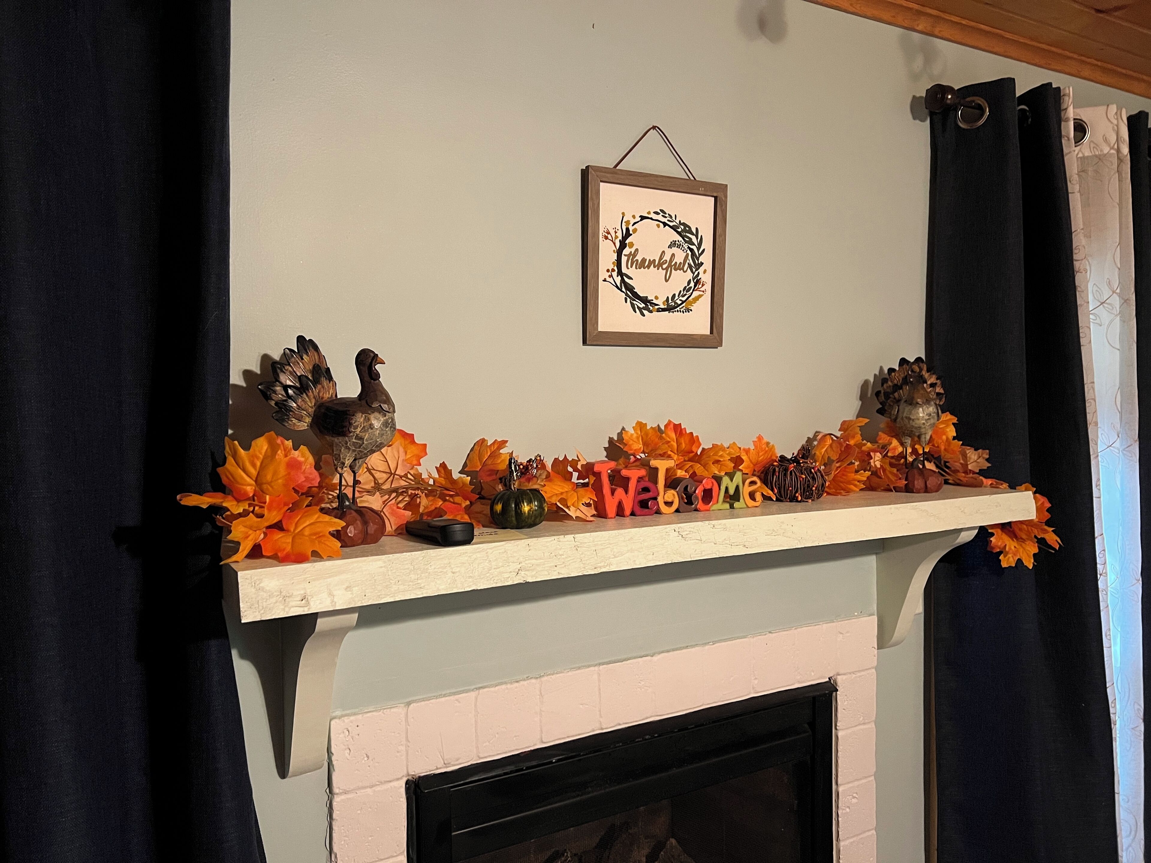 Une cheminée ornée d’une console décorée de feuilles d’automne, d’une pancarte « Bienvenue » et d’un cadre avec l’inscription « Merci ».