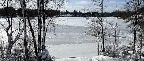 Un lac gelé, bordé d’arbres couverts de neige, avec une clôture en bois au premier plan.