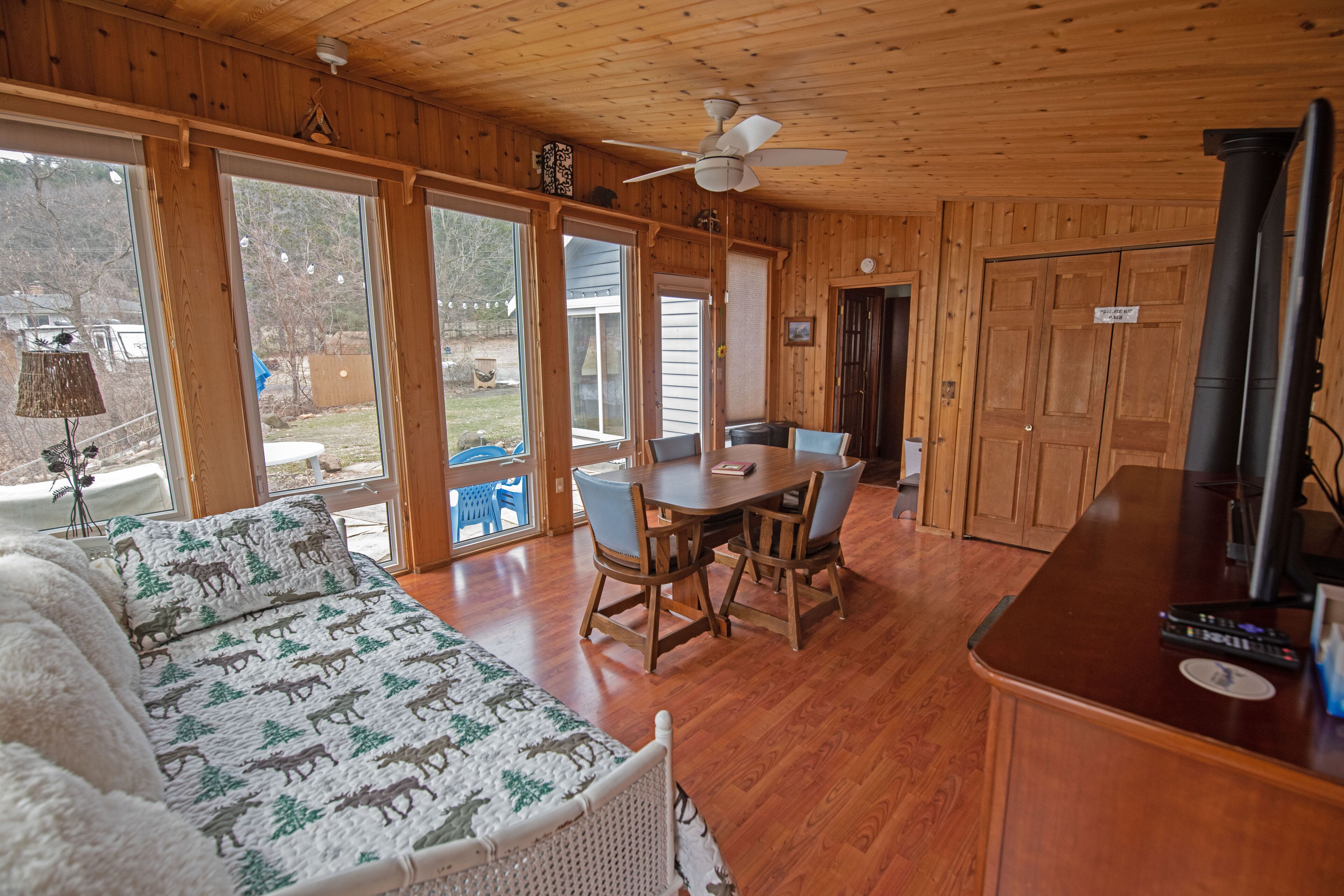 A wooden cabin interior with a sofa, dining table, chairs, and a kitchen area.