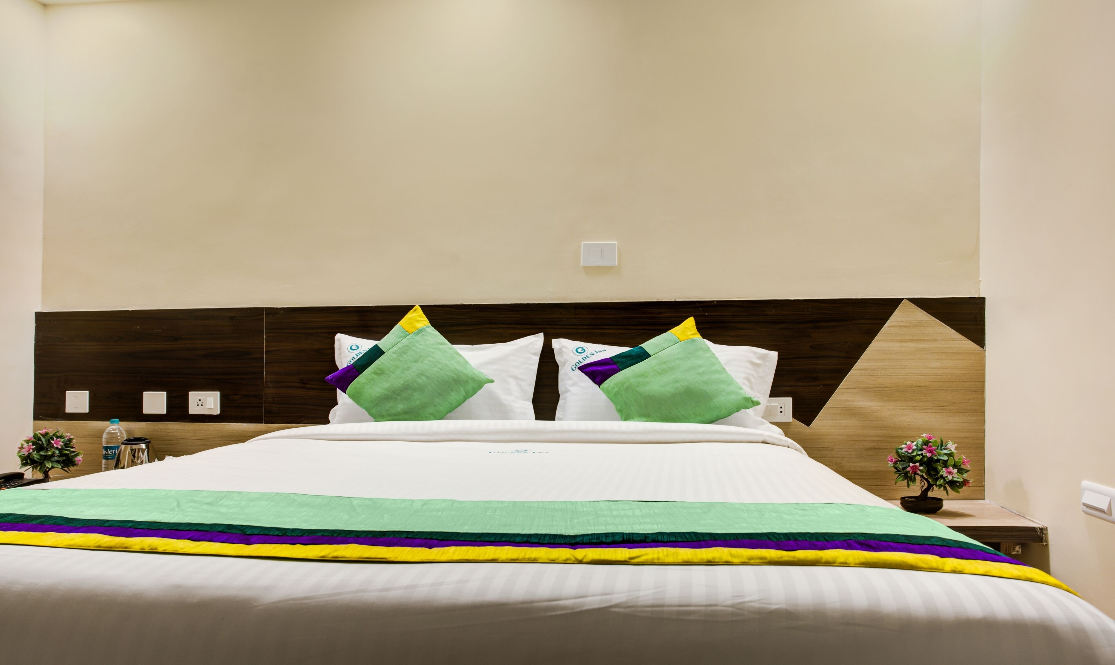 A neatly made bed with a striped bedspread, two pillows with a green and white design, and a wooden headboard.