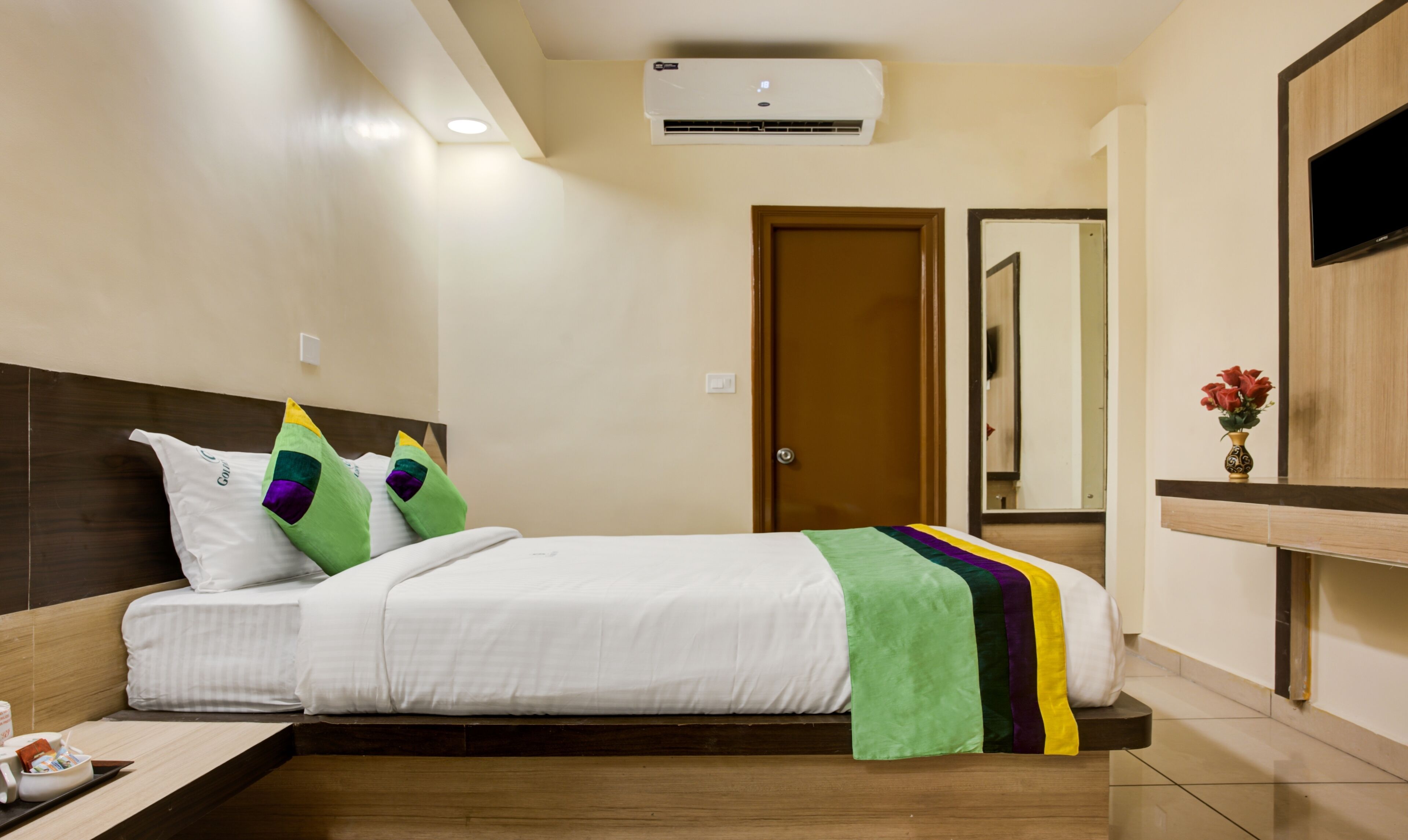 Una habitación de hotel con una cama, una mesita de noche con lámpara, un televisor y un espejo.