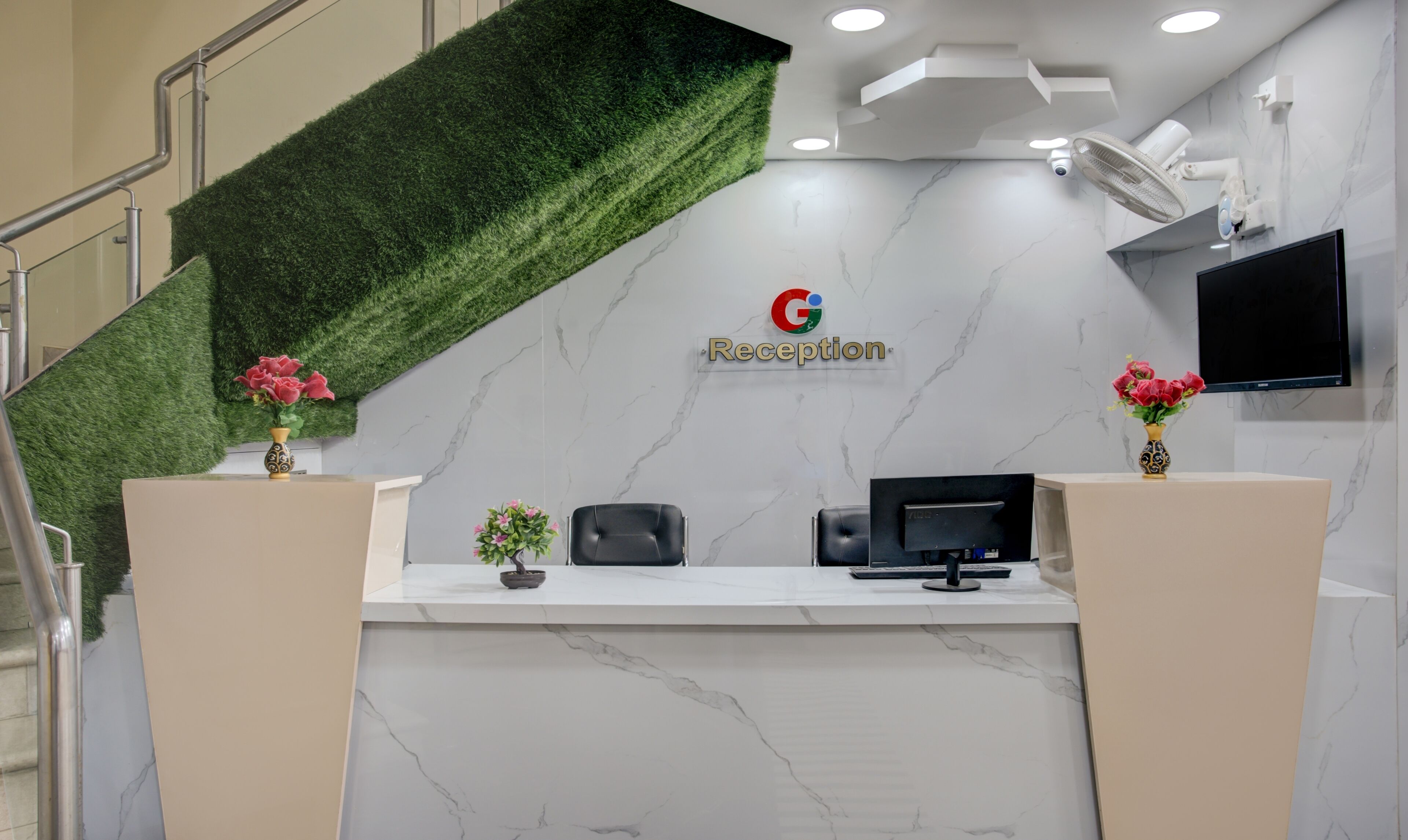 Un mostrador de recepción con una pared de césped artificial verde, el logotipo de Google y un televisor de pantalla plana.