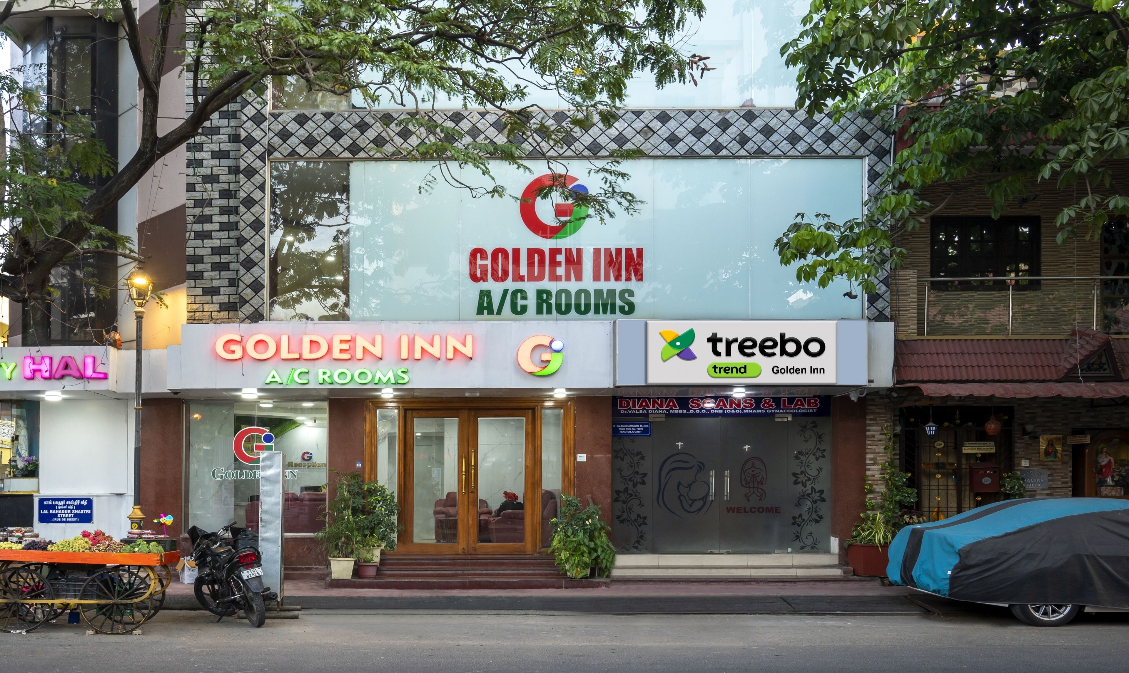 Un hotel llamado Golden Inn con habitaciones con aire acondicionado, una recepción visible y un carrito de frutas cerca.