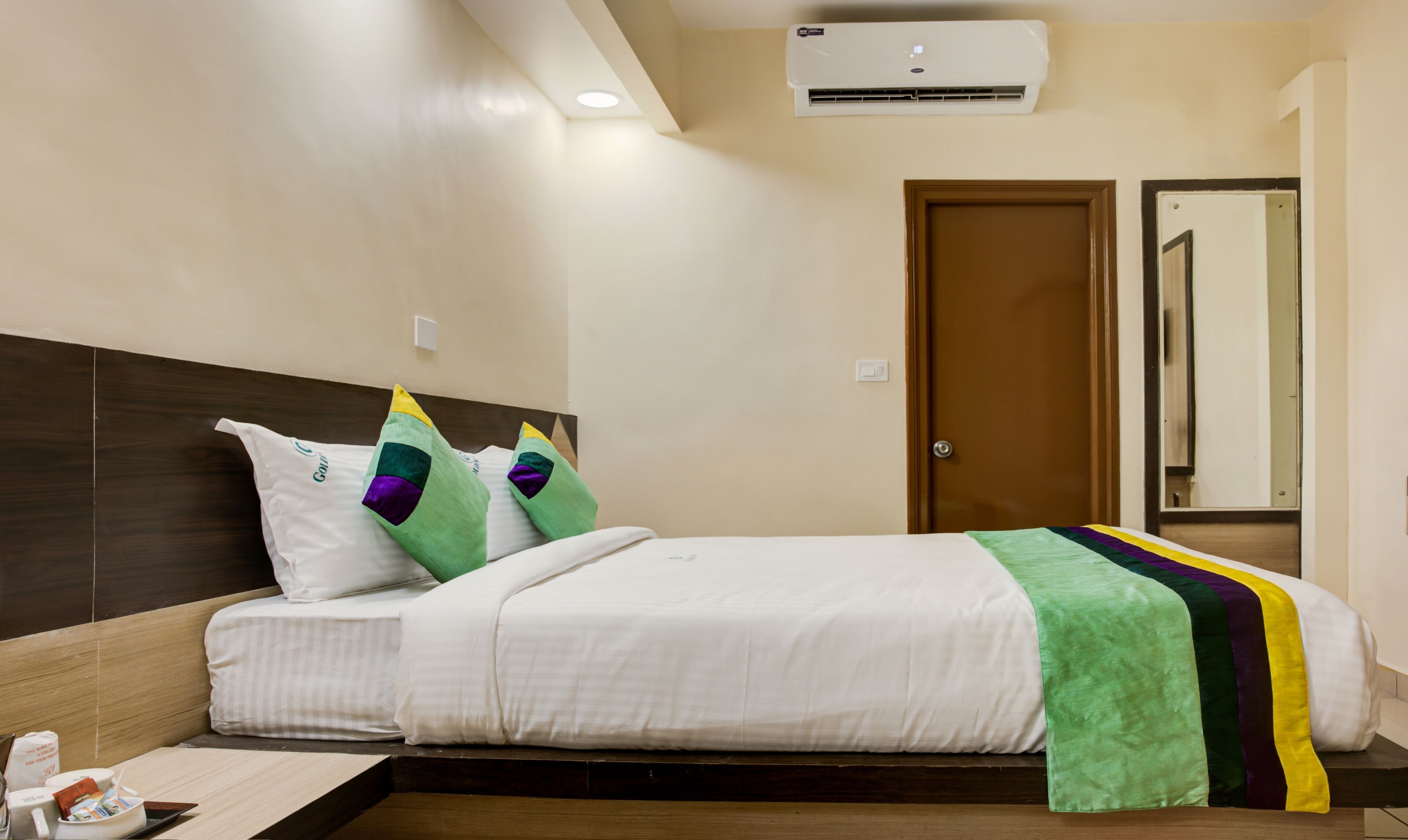 Una habitación de hotel con cama, almohadas, una mesita de noche y un espejo.