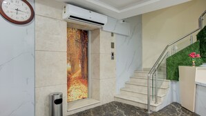 A modern hotel lobby with a marble floor, a staircase with glass railings, and a wall-mounted air conditioning unit. - Treebo Golden Inn, 700 Mtrs From Promenade Beach (Puducherry)