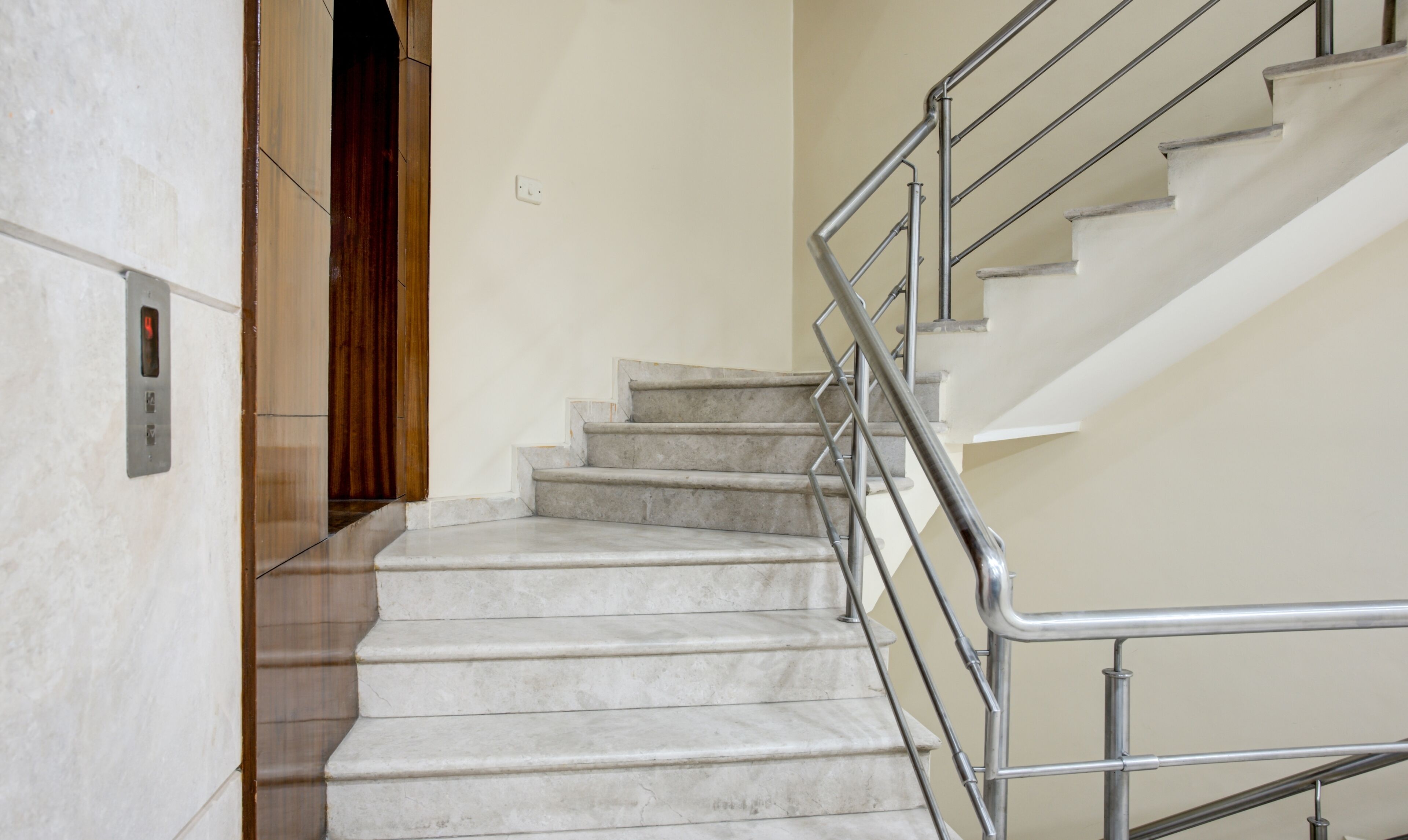 A staircase with a metal railing, marble steps, and a wooden door at the top.