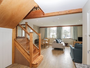 A spacious living area with a wooden staircase, a stone wall, a sofa, and a television. - The Old Haberdashery (Swanage)