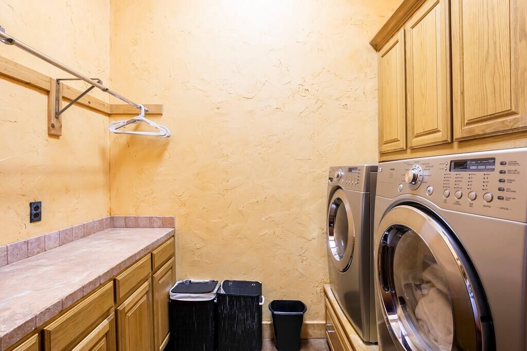 Une petite buanderie comprenant un lave-linge, deux poubelles, des placards en bois et un porte-serviettes.