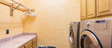 Une petite buanderie comprenant un lave-linge, deux poubelles, des placards en bois et un porte-serviettes.