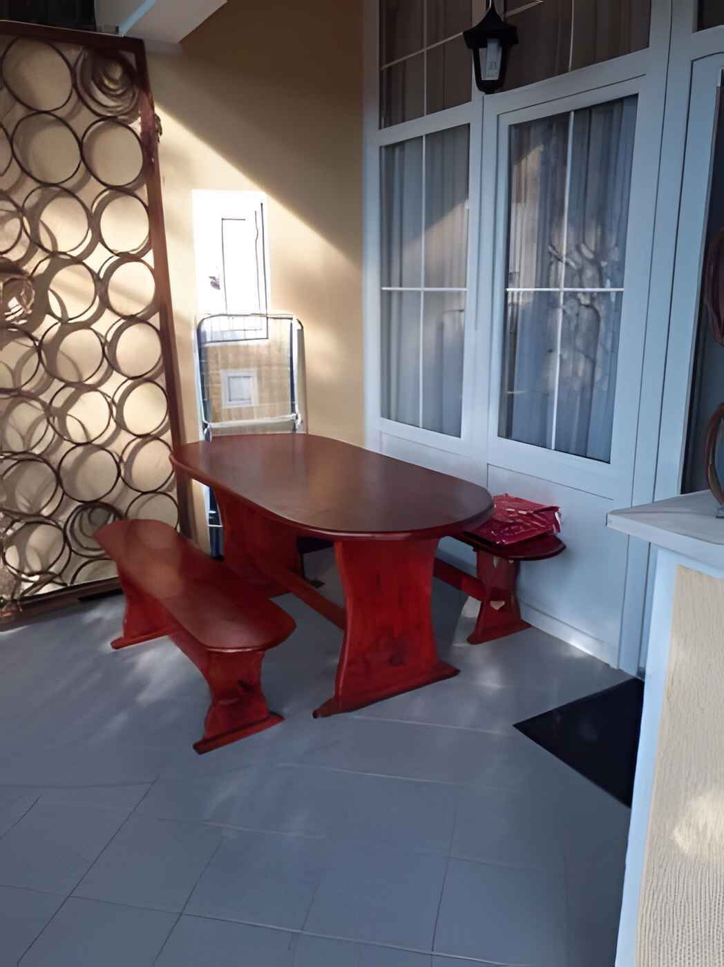 A dining area with a wooden table and benches, a decorative metal partition, and a window with curtains.