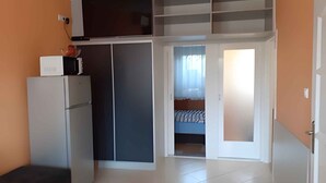 A compact living space with a kitchenette, a bed, and a sliding door leading to a balcony.