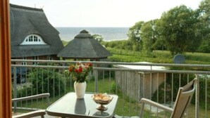 Een balkon met een tafel, een bloevas en uitzicht op een huis en de zee.
