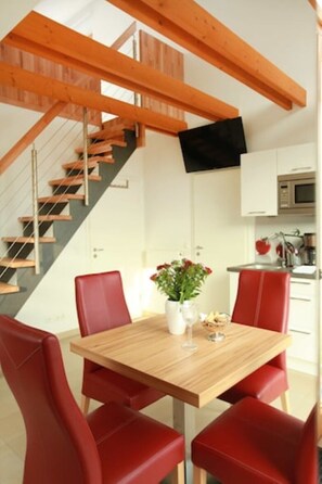 A dining area with a wooden table and red chairs, a staircase with wooden beams, and a kitchen with white cabinets and a microwave.