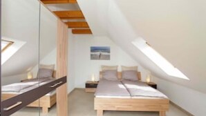 A bedroom with two beds, wooden headboards, a skylight, and a small bedside table with a lamp.
