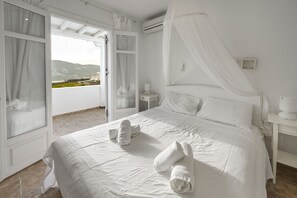 Une chambre d’hôtel avec un grand lit, des rideaux blancs, une table de chevet et une vue sur l’extérieur.