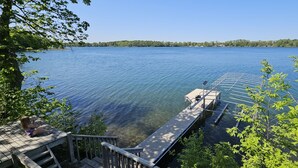 A wooden dock extending into a calm lake with clear water, surrounded by trees and a distant shoreline. - Beautiful lake house with pontoon INCLUDED! (Vergas)