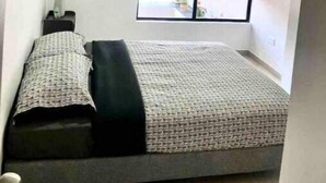 Une petite chambre à coucher moderne, équipée d’un lit, d’une table de chevet, d’une fenêtre avec vue et d’un appareil de climatisation.