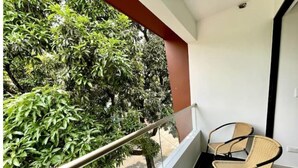 Un balcon avec deux fauteuils en osier, une rambarde en métal et une vue sur un feuillage verdoyant et luxuriant.