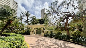 Una entrada ajardinada con un paseo techado, palmeras y un área amurallada.