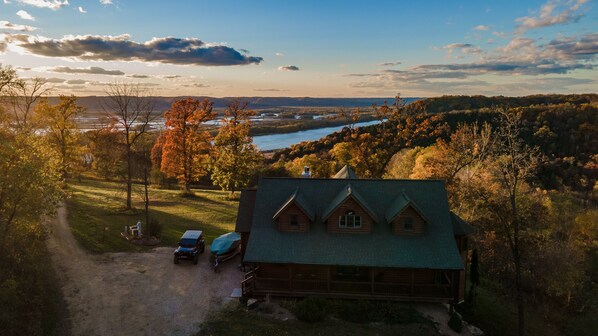 A cabin with a green roof, surrounded by trees and a river.