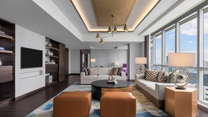 Un salon moderne doté d’un grand téléviseur à écran plat, d’une table basse ronde et d’un canapé assorti de deux poufs. On y trouve également deux lampadaires et un luminaire au plafond.