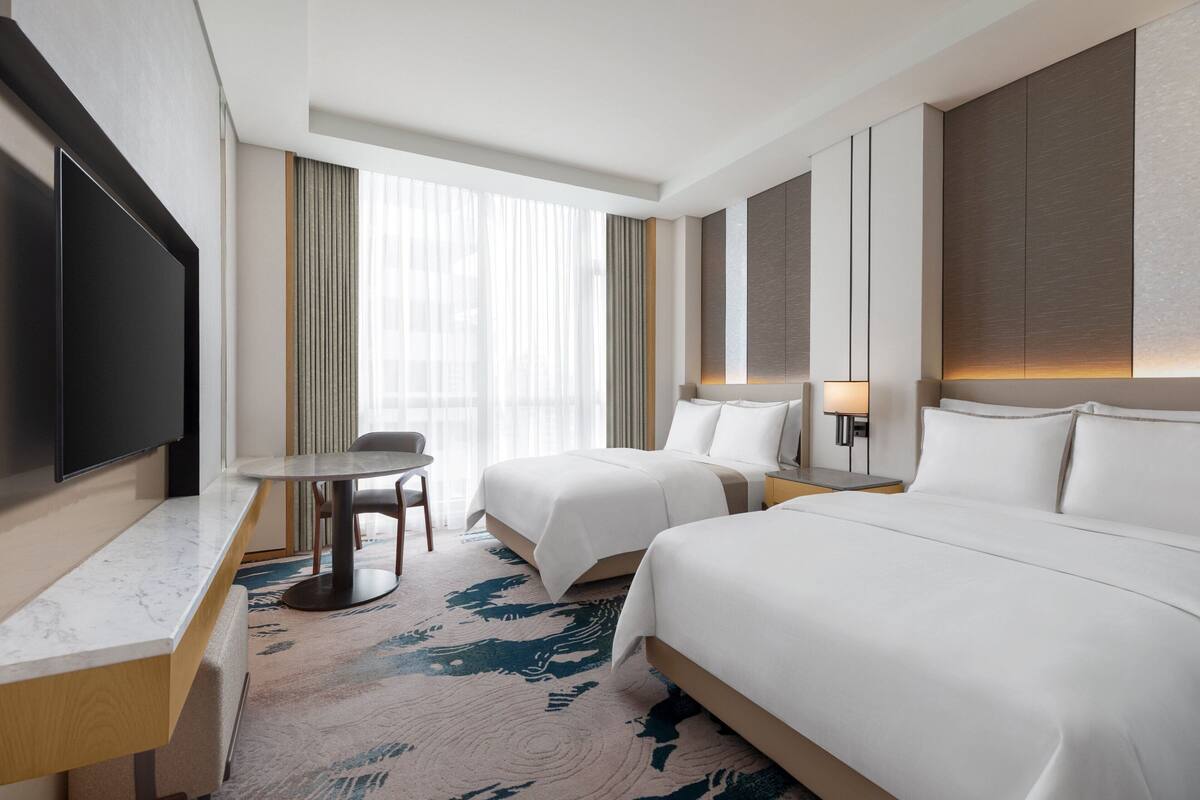 Une chambre d’hôtel avec deux lits, un bureau, une télévision et une fenêtre avec des rideaux.