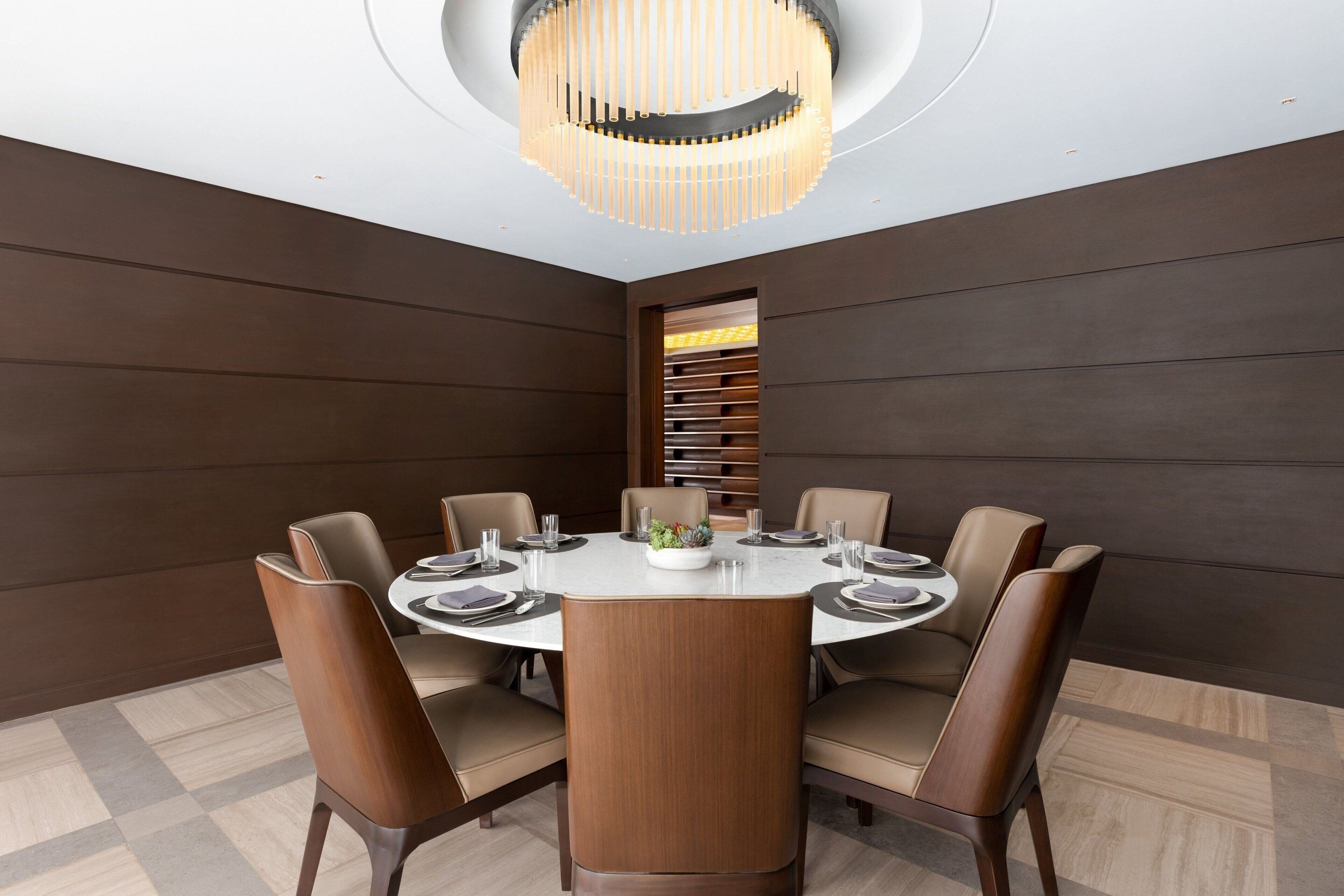 A modern dining room with a round table, six chairs, and a central chandelier.
