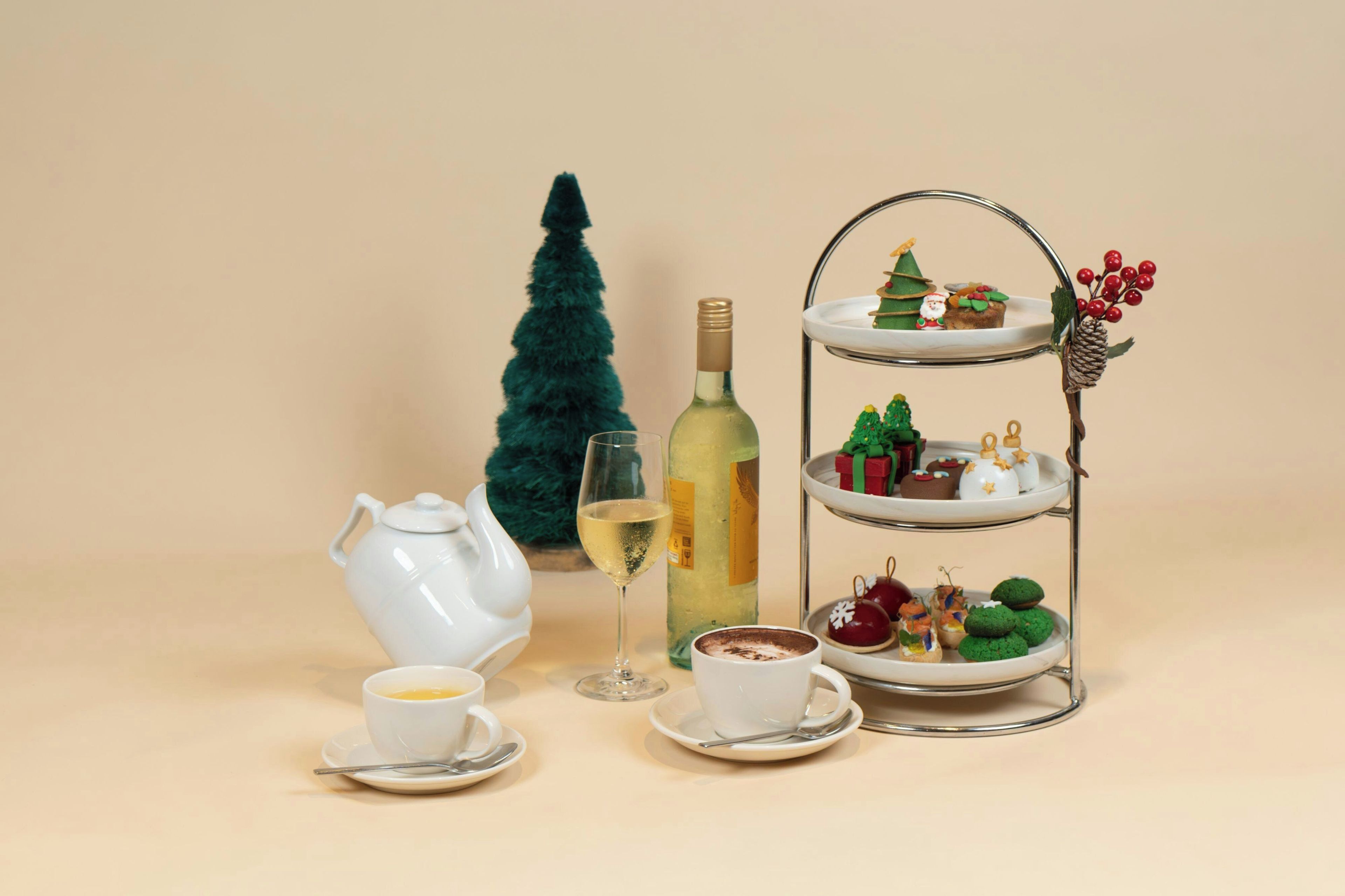 Ein Teeservice mit Teekanne und Tassen, eine Weinflasche, ein Weinglas, eine Etager mit verschiedenen Süßigkeiten und ein Weihnachtsbaum.