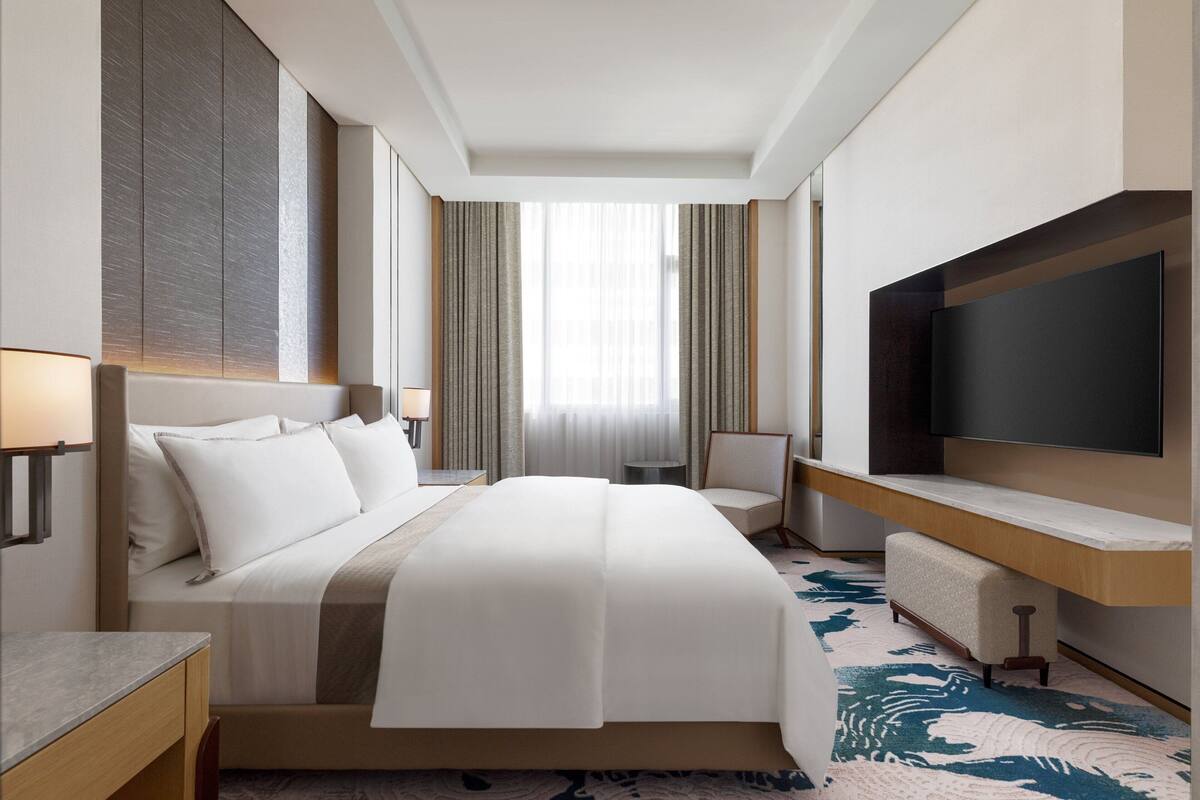 Une chambre d’hôtel dotée d’un grand lit, d’un téléviseur à écran plat, d’un bureau avec une chaise et d’une fenêtre avec des rideaux.