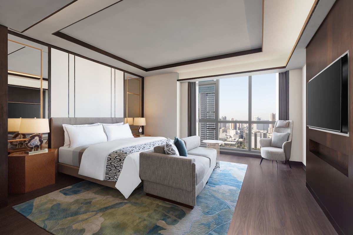 Une chambre d’hôtel moderne avec un grand lit, un canapé, une télévision et une vue sur la ville.