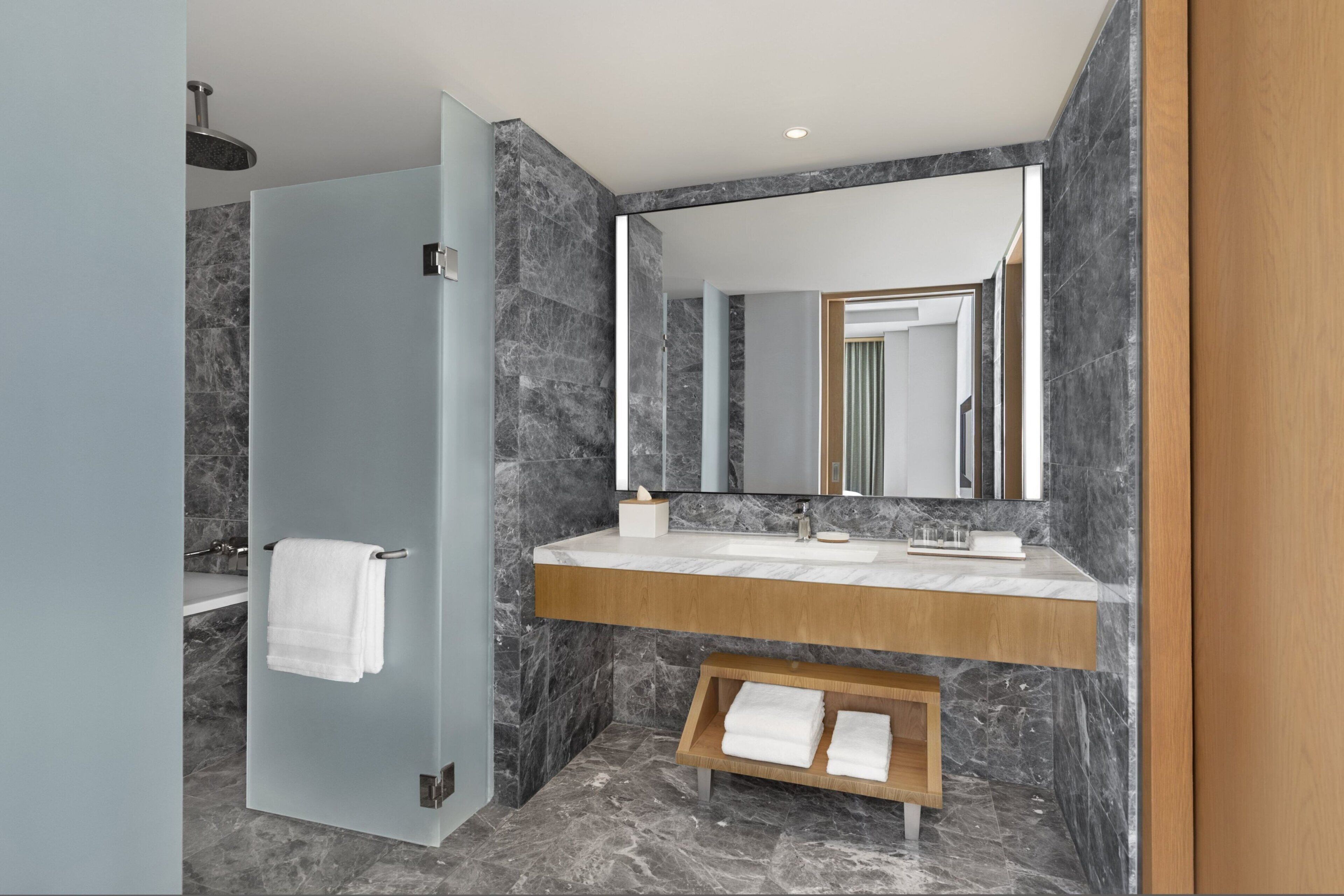 Une salle de bain moderne avec un sol en marbre, un meuble-lavabo en bois, un grand miroir et une cabine de douche en verre.
