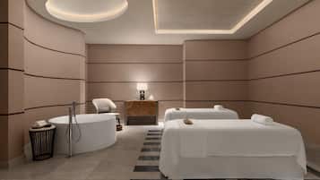 Ein modernes Hotelzimmer mit einer großen Badewanne, zwei Betten, einem Schminktisch mit Spiegel und einer kleinen Sitzecke.