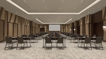 Ein geräumiger Konferenzraum mit mehreren Tischen und Stühlen, einer großen Leinwand und einem gemusterten Teppich.