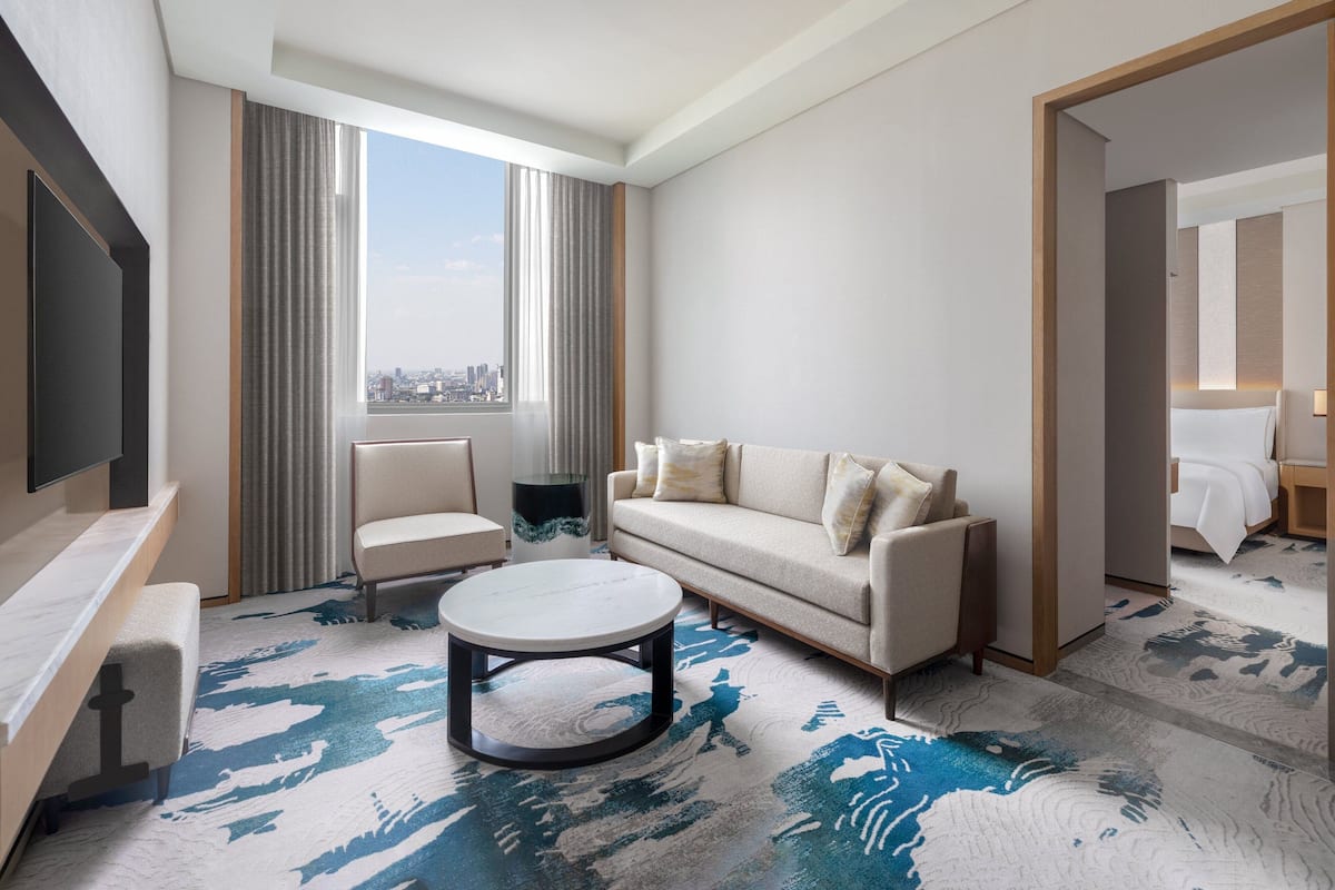 Une chambre d’hôtel moderne dotée d’une grande fenêtre, d’un canapé, d’un fauteuil, d’une table basse et d’un téléviseur.