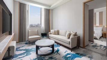 Ein modernes Hotelzimmer mit großem Fenster, einer Couch, einem Sessel, einem Couchtisch und einem Fernseher.