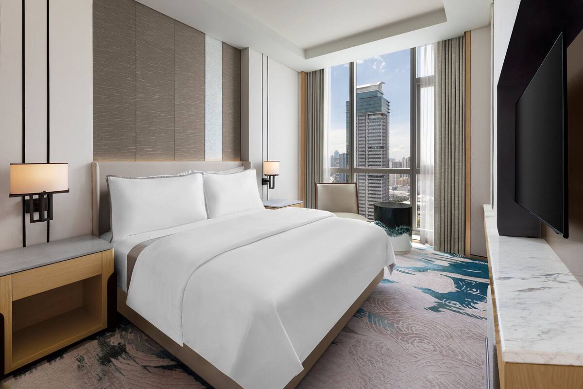 Une chambre d’hôtel moderne dotée d’un grand lit, d’une télévision à écran plat, d’une vue sur la ville et d’un mur décoratif en marbre.