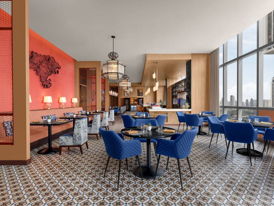 A modern hotel lobby with a central seating area, a bar, and large windows offering a city view.
