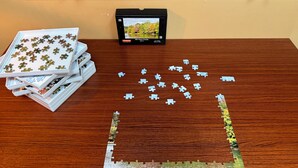 A wooden table with puzzle pieces, a framed photo, and a small device.