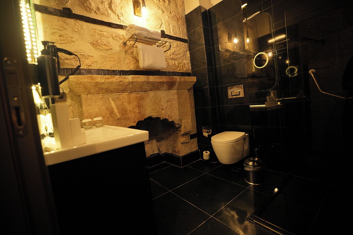 Un baño moderno con una pared de acento de piedra, un lavamanos blanco, un inodoro y un box de ducha de vidrio.