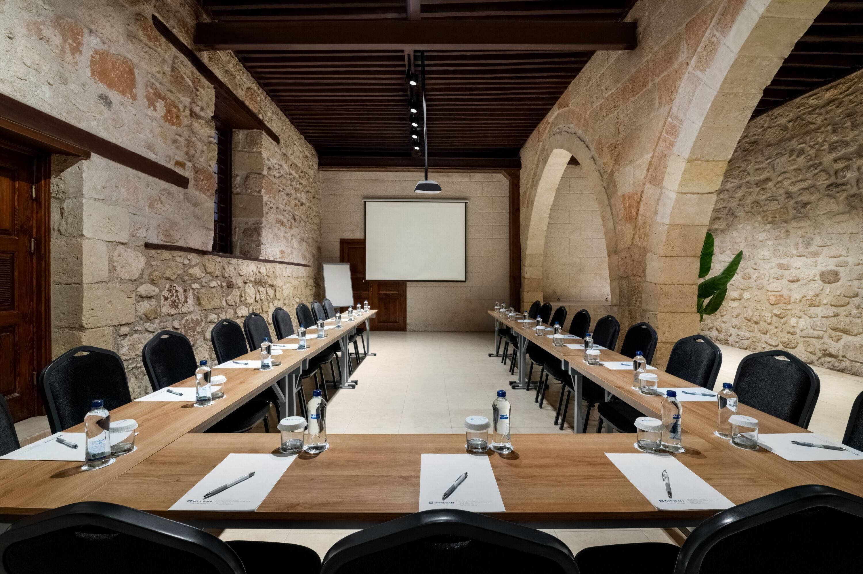 Een vergaderzaal met een lange tafel, stoelen en een projectiescherm.