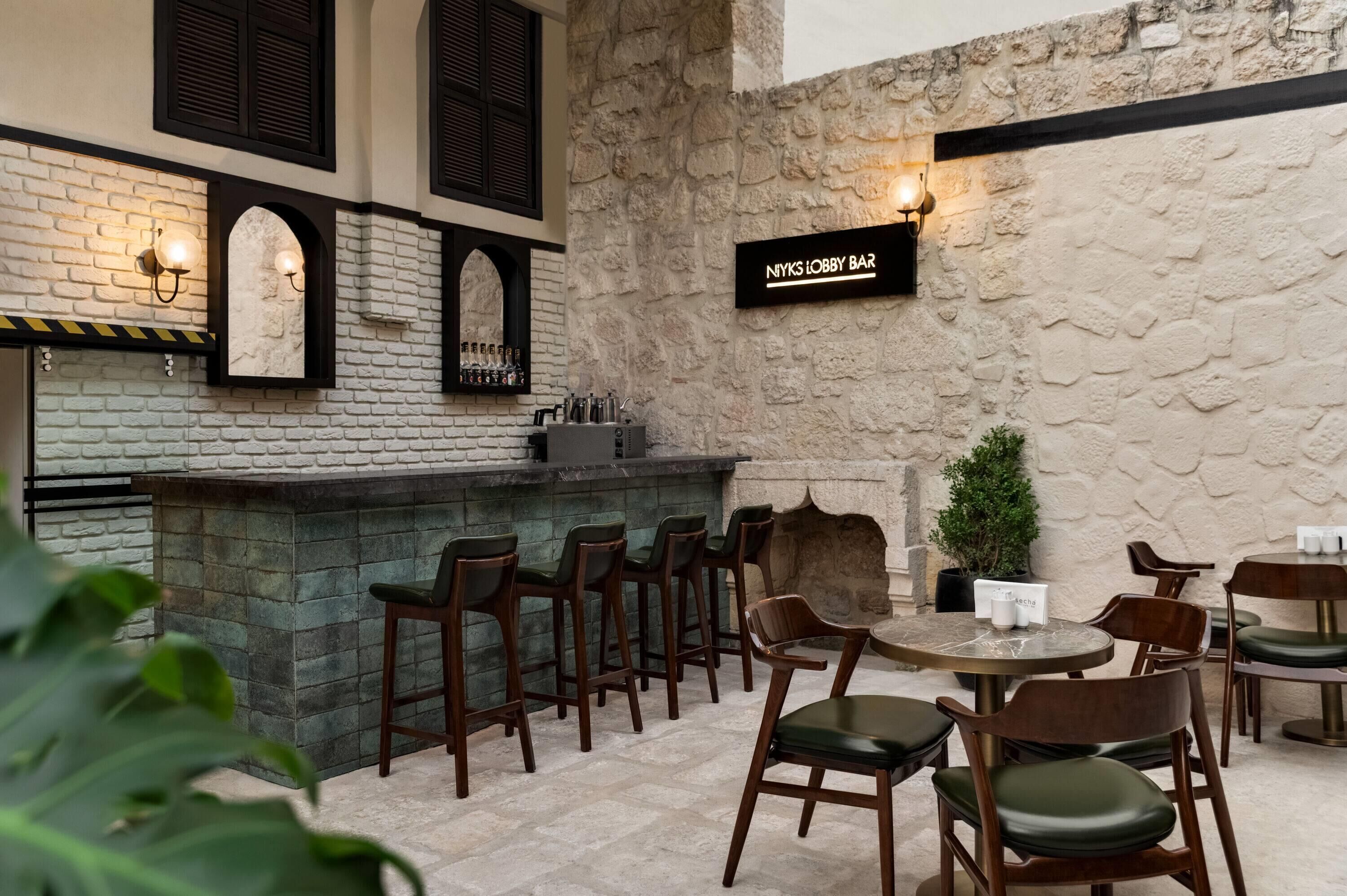 Una zona de bar con pared de piedra, sillas de madera y un letrero que dice 'NIYKS LOBBY BAR'.