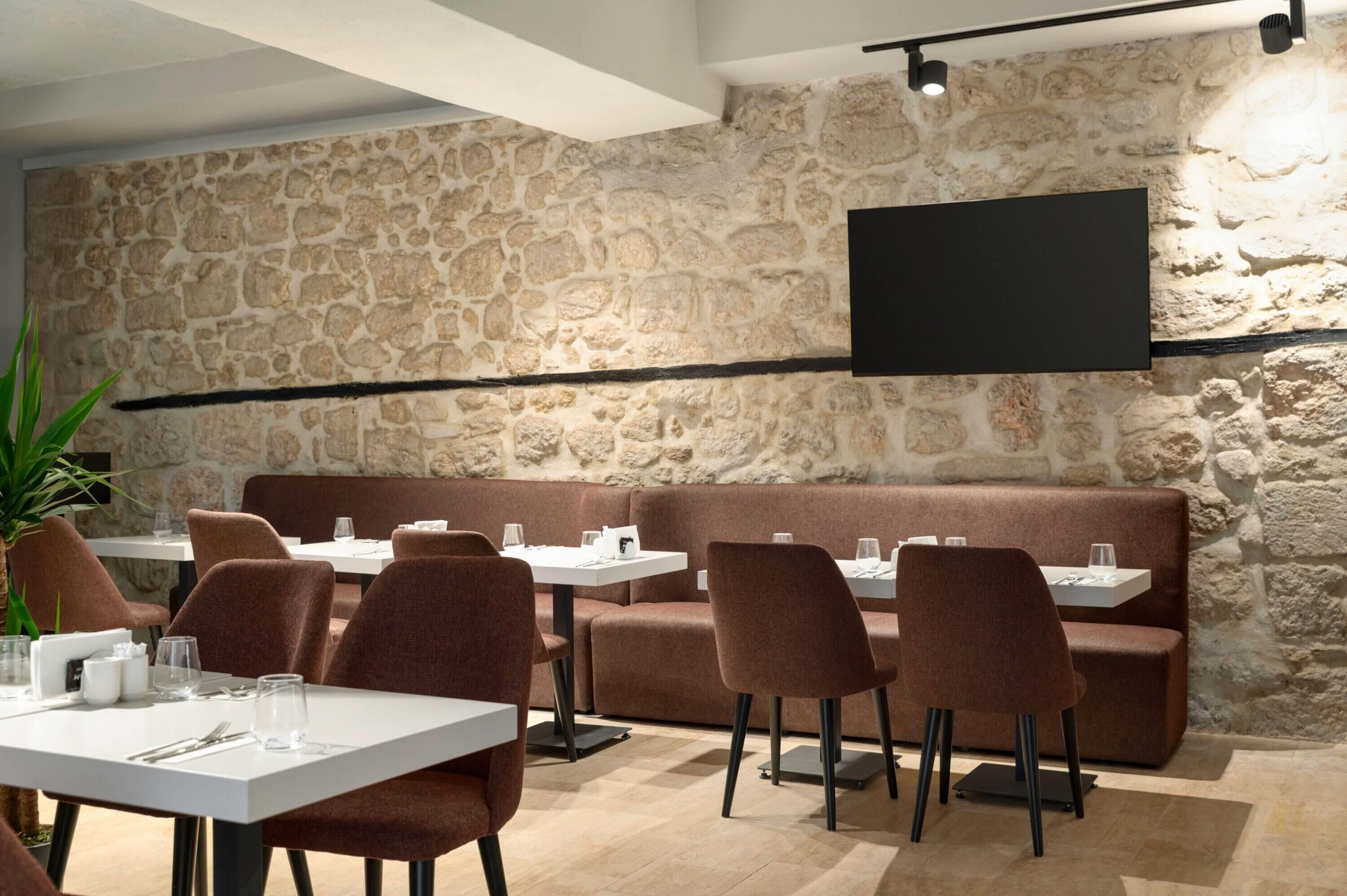 Un restaurante con paredes de piedra, un televisor de pantalla plana montado en la pared y una zona de estar con mesas y sillas.