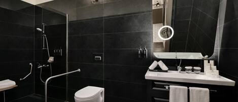 A modern bathroom with a black tiled wall, a white toilet, a sink with a mirror, and a shower area with a handheld showerhead.
