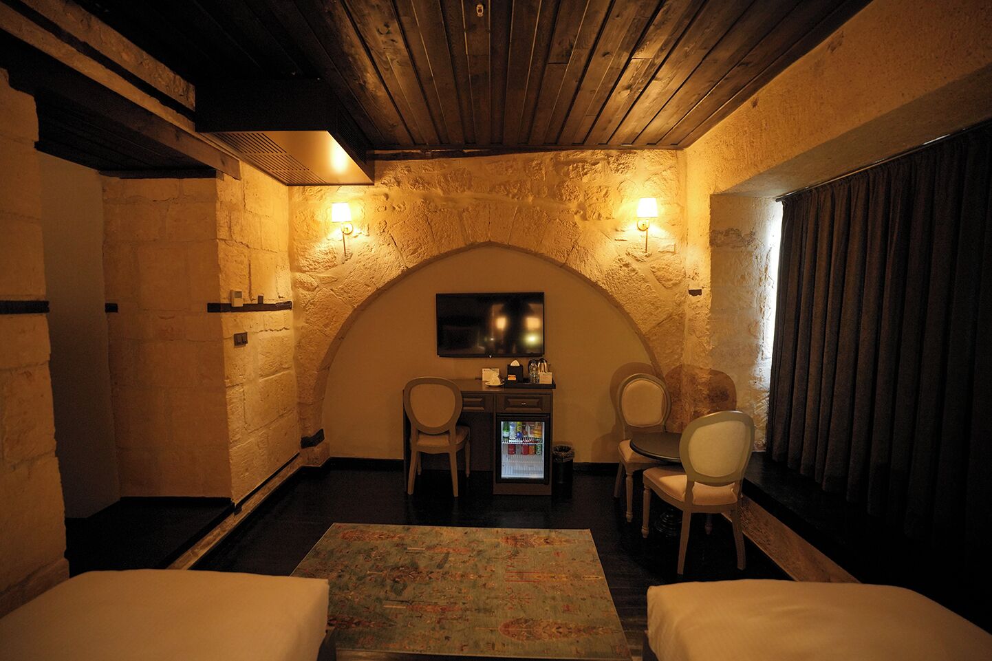 Una habitación acogedora con pared de piedra, techo de madera, dos camas, una mesita con sillas y un televisor.
