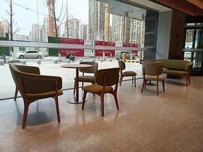 Un intérieur moderne avec un espace salon comprenant des tables et des chaises rondes, de grandes fenêtres offrant une vue sur un paysage urbain avec des immeubles de grande hauteur et une rue animée.