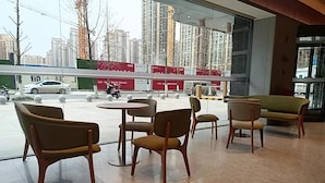 Een modern interieur met een zithoek, bestaande uit ronde tafels en stoelen, grote ramen met uitzicht op een stadsbeeld met wolkenkrabbers en een straat met voertuigen.