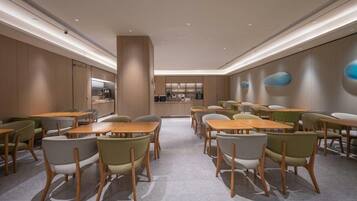 A modern dining area with wooden tables and chairs, a kitchen in the background, and a minimalist design.